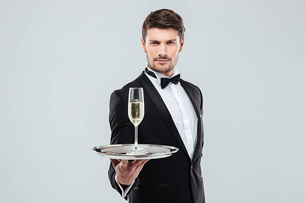 タキシードの魅力的な若い執事はあなたにシャンパンのグラスを提供しています - butler champagne service waiter ストックフォトと画像