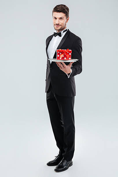 istock Butler in tuxedo standing and holding tray with gift box 585770890