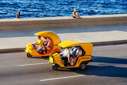 Havana, Cuba - March 17, 2015: Coco Taxis driving along the Malecon in Havana, Cuba. The three wheeled vehicle  is a common form of public transportation in the city of Havana Cuba.