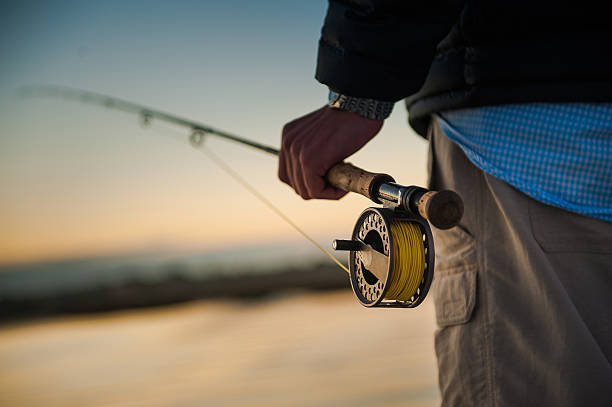 Man holding fly rod Sunrise over the marsh with man holding a fly rod and reel fly fishing stock pictures, royalty-free photos & images