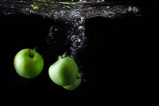 istock Three green apples splashing into water on black background. 585774186