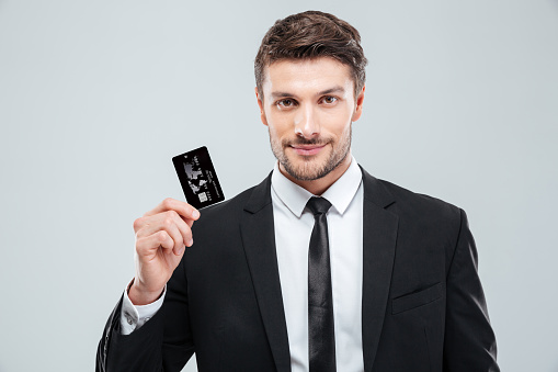 Portrait of handsome young businessman holding credit card over white background