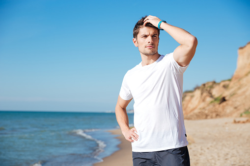 Closeup of attractive young man in white t-shirt standing and thinking on the beach