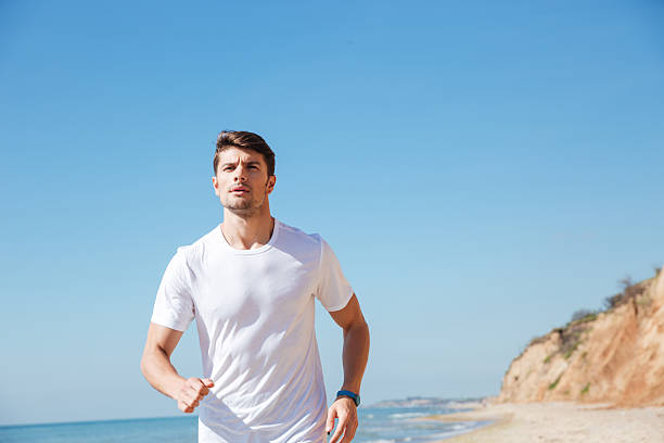 istock Confident young sportsman jogging on the beach 585778960
