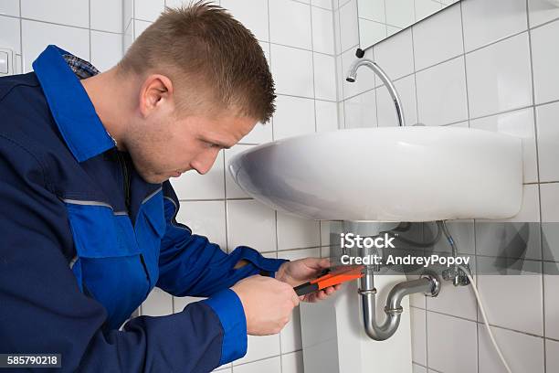 Male Plumber Fixing Sink In Bathroom Stock Photo - Download Image Now - Repairing, Bathroom, Bathroom Sink
