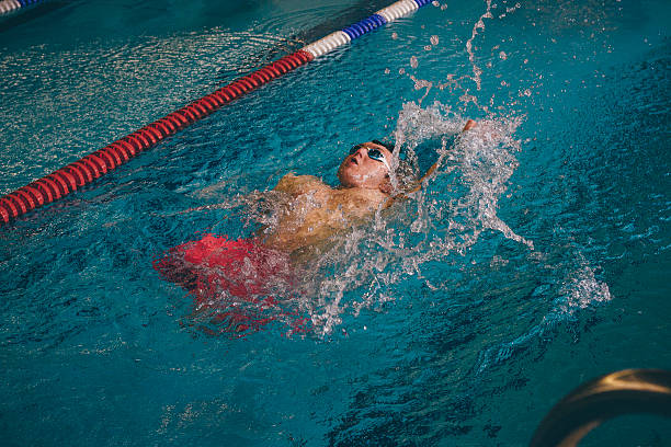 Quadriplegic swimmer in the water. He is using the back stroke technique in the pool lane.
