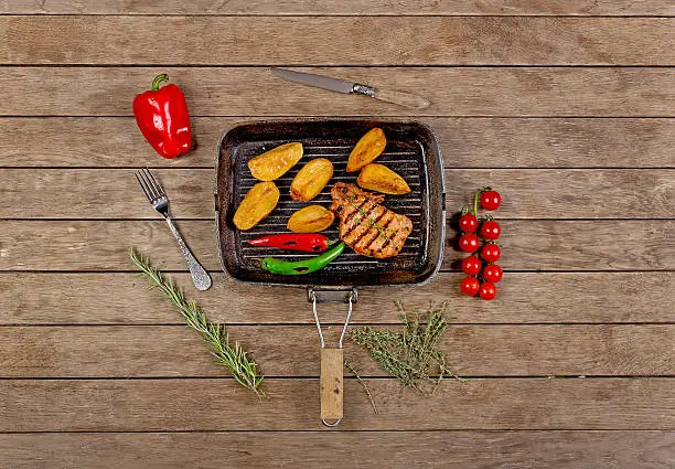 roast chicken and potatoes on the grill in a cast iron skillet on wooden background top view