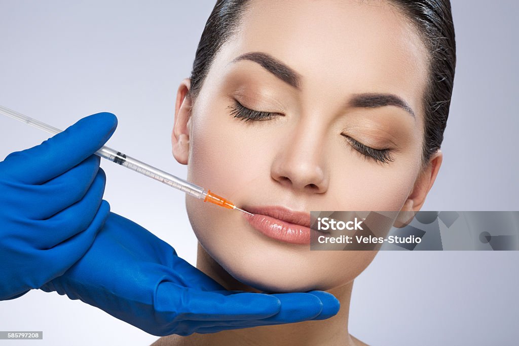Young model having plastic operation Young lady with closed eyes. Lips operated by plastic surgeon. Beauty injection by doctor in blue gloves. Beauty portrait, closeup. Indoor, studio Botulinum Toxin Injection Stock Photo
