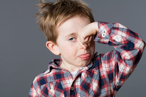 annoyed young child pinching his nose for sign of bad smell, sticking out his tongue for cheeky humor and mischievous childhood, grey background