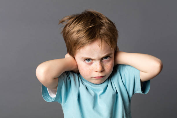 stubborn kid with an attitude ignoring parents scolding, blocking ears stubborn little kid with red hair, freckles and an attitude ignoring parents scolding, blocking his ears with hands against education problems, grey background Rudeness stock pictures, royalty-free photos & images