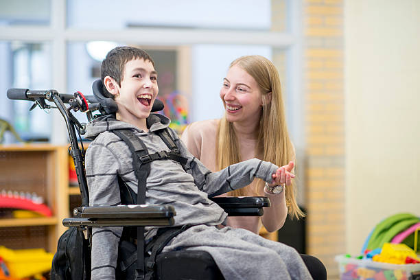 Bond Between Caregiver and Patient A caregiver is playing with a little boy that has a mental and physical disability. He is happily sitting in his wheelchair. disability stock pictures, royalty-free photos & images