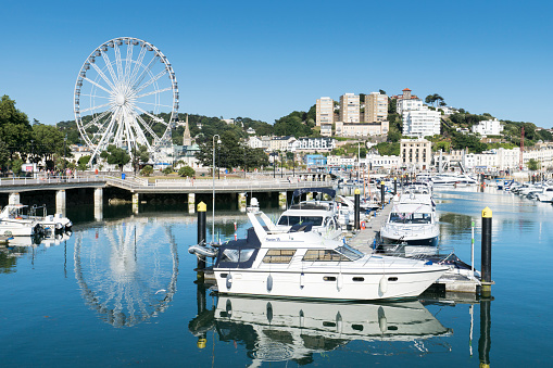 Torquay,England - July 22, 2016: Torquay marina in south Devon with lots of expensive boats on view and a big wheel taking tourists for a ride. The harbour front can be seen with hotels up on the hill. Some people can be seen walking around.