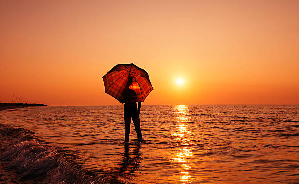 istock Young boy with umbrella on the beach at sunrise 585804982