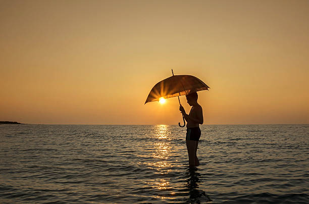 istock Young boy with umbrella on the beach at sunrise 585805032