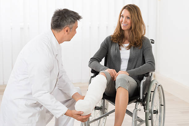 Physiotherapist Examining Leg Of Patient Physiotherapist Examining Leg Of Patient Sitting On Wheelchair man sitting with a bandage on his leg stock pictures, royalty-free photos & images