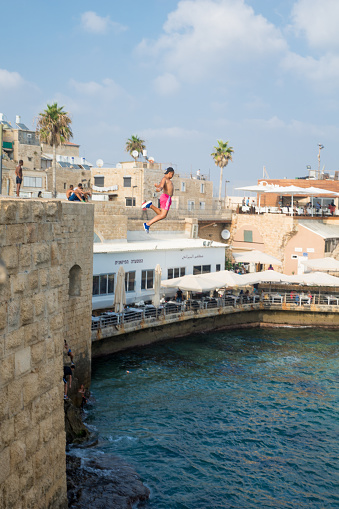 Acre, Israel - August 3, 2016: Young man jumps to the sea from the top of the ancient walls of Acre, Israel. Acre is one of the oldest continuously inhabited sites in the world