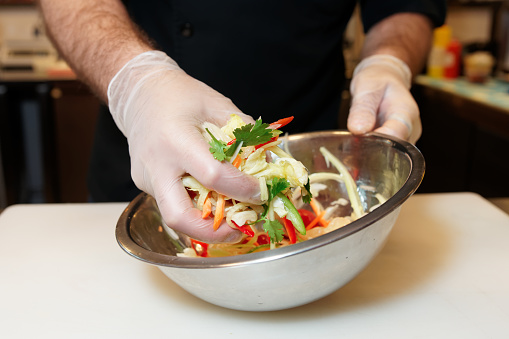 Chef is mixing a vegetarian salad in stainless steel bowl