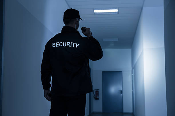 Security Guard With Flashlight In Building Corridor Rear view of security guard with flashlight in building corridor security guard photos stock pictures, royalty-free photos & images
