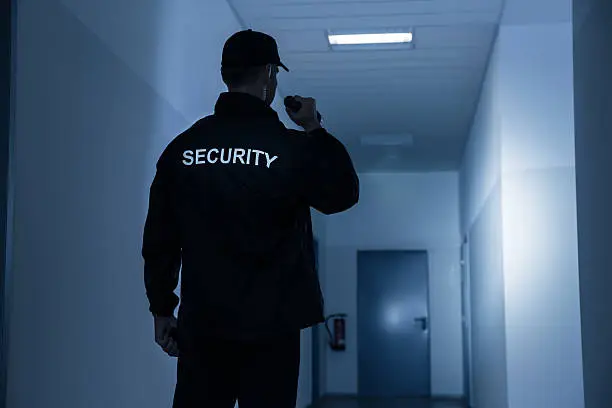 Rear view of security guard with flashlight in building corridor