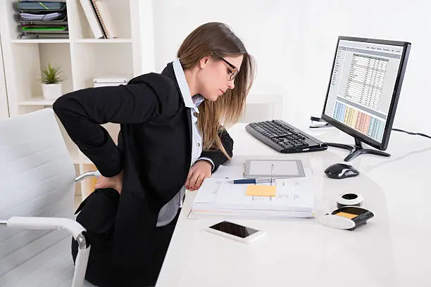 Young Businesswoman With Backpain Sitting On Chair At Workplace