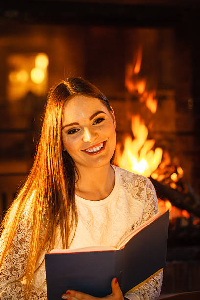 istock Smiling woman reading book at fireplace. Relax. 586045688
