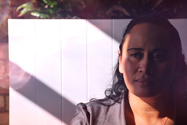 A Maori Lady looks to distance as she sits in sunlight of Boardroom.