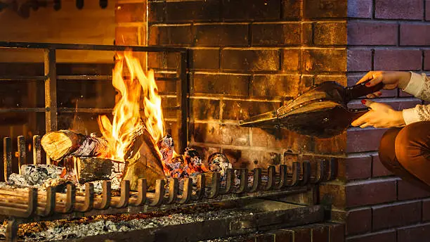 Closeup of human hands at fireplace making fire with bellows. Person heating warming up and relaxing. Winter at home.