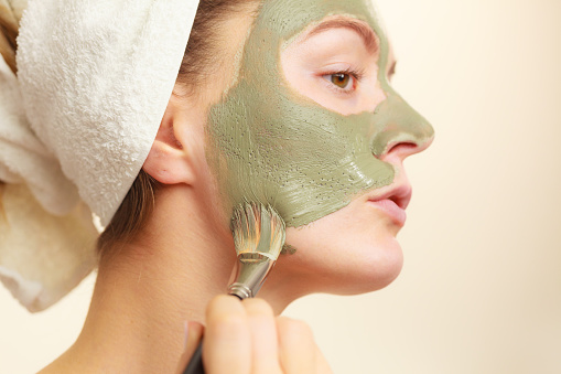 Skin care. Woman applying with brush clay mud mask to her face. Girl taking care of oily complexion. Beauty treatment.