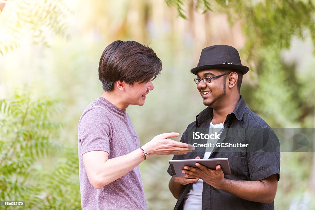Dude, this is the new app which I developed. Asian teenager boy showing his newly developed app on a digital tablet to his friend. Digital Tablet Stock Photo