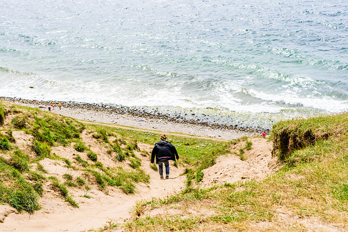 Kaseberga, Sweden - August 1, 2016: Real people in everyday life. Young adult man walking or sliding down a sandy path on a hillside toward the ocean below.