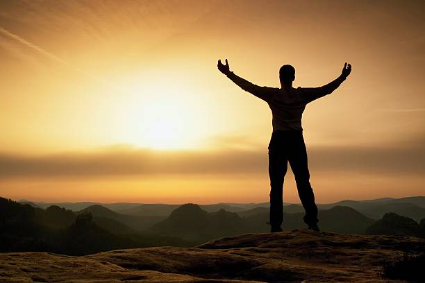 Happy man with open raised arms Gesture of triumph. Satisfy hiker  silhouette on sandstone cliff watching down to landscape.