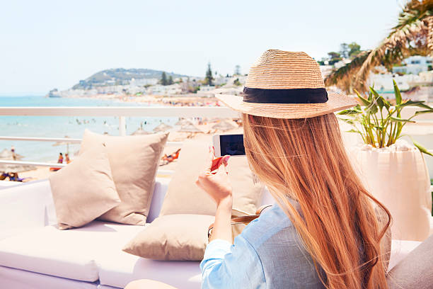 Happy young blond woman taking smartphone photo with smart phone Happy young blond woman taking smartphone photo with smart phone of a beach in Gammarth Tunis, Tunisia on outdoor patio sofa furniture tunisia beach stock pictures, royalty-free photos & images