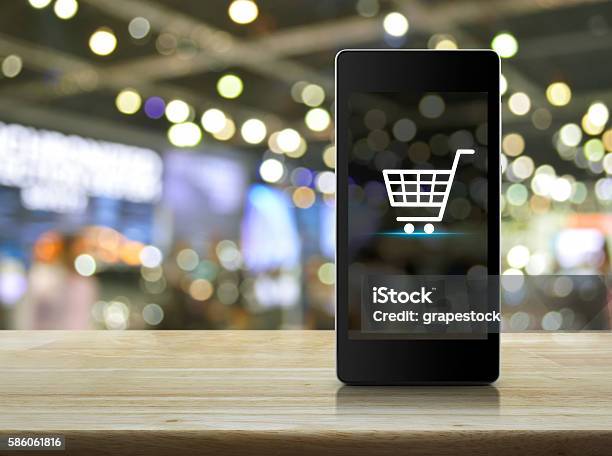 Shopping Cart Icon On Smart Phone Screen Over Blur Mall Stock Photo - Download Image Now