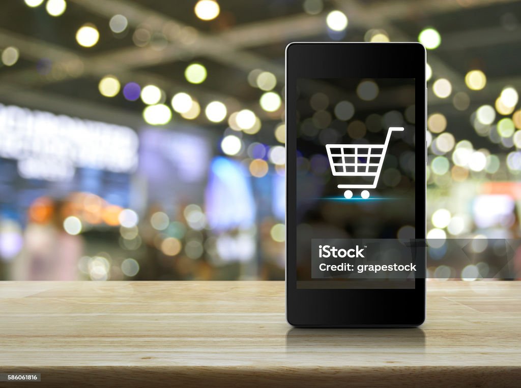 Ícone do carrinho de compras na tela do telefone inteligente sobre shopping desfocado - Foto de stock de E-commerce royalty-free