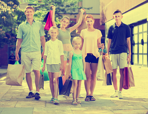 Smiling young parents with four kids gladly shopping in town