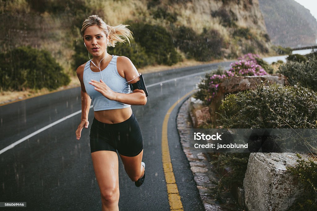 Female athlete running outdoors on highway Female athlete running outdoors on highway. Beautiful young woman training running on a rainy day. Running Stock Photo
