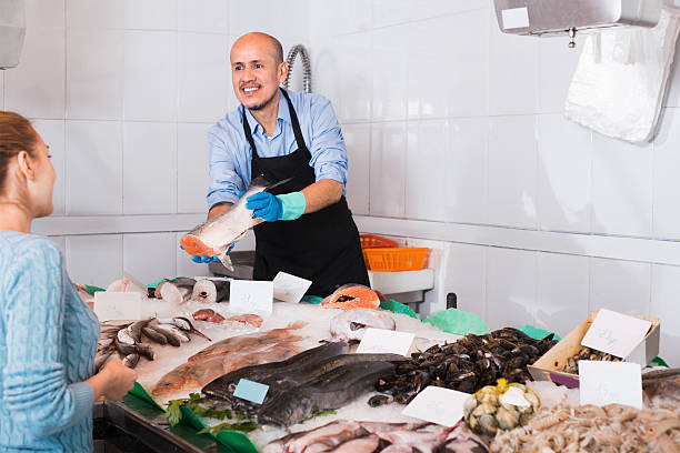 istock Mature smiling seller helping female customer to choose fish 586072448