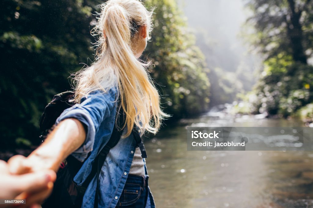 Couple crossing the creek holding hands Young woman leading her boyfriend on the forest hike. Point of view shot of couple crossing the creek holding hands. Nature Stock Photo