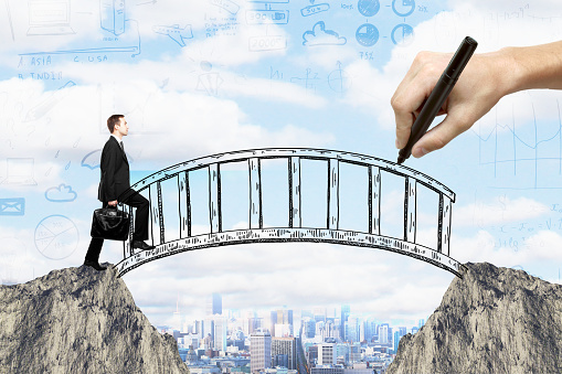 Success concept with hand drawing bridge over gap between two cliffs and businessman walking across it on city background with business sketches