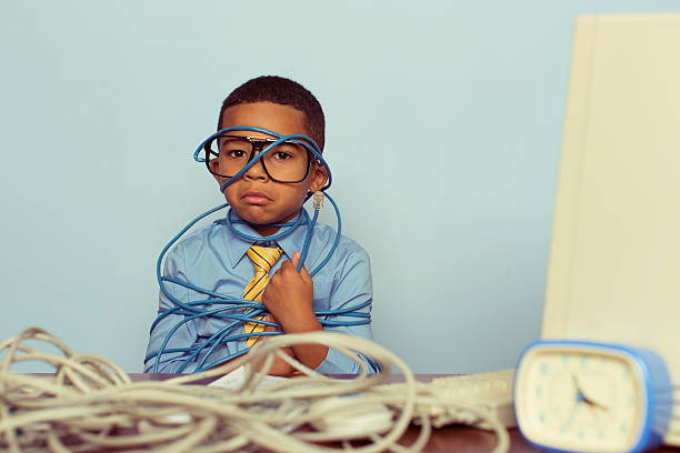 A young IT professional sadly looks over a large pile of tangled internet cables on his desk. He is dressed in a blue shirt, tie and glasses while looking over worked and tired in front of light blue background. Retro styling. 