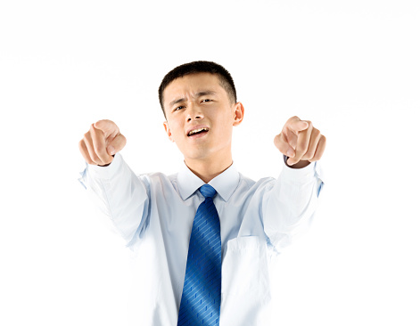 Young asian businessman pointing at camera against white background.
