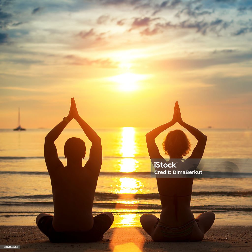 Silhouettes of young couple practicing yoga on the beach Silhouettes of young couple practicing yoga on the beach during sunset. Beach Stock Photo