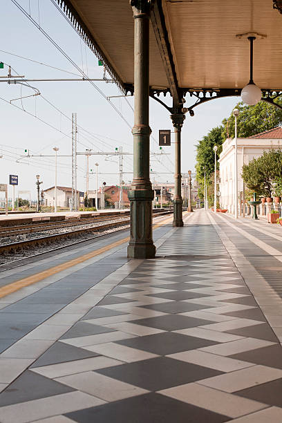 Taormina/Giardini, Sicily, Italy-4th October 2011: Train station platform looking south showing two columns and roof of the 19th century construction. The tiling on the platform floor is also visible in the vertical composition. The train tracks are visible to the left of frame. The cloudless sky is pale blue with morning light. No people are present.