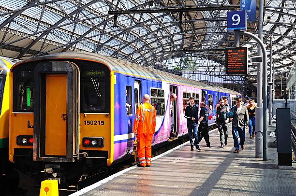 Medium shot of trains lined up inside a railway station in Glasgow, Scotland. There are people walking along the platform and sunlight filtering through the glass roof.