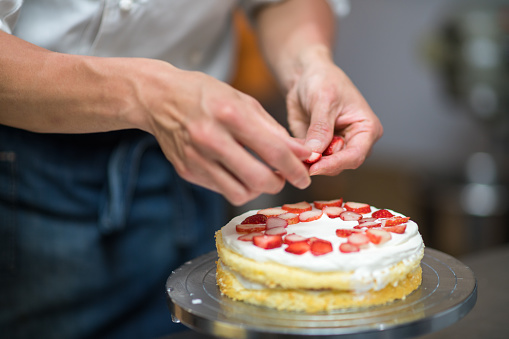Baker adding strawberries in between layers on a cake he is making. Kyoto, Japan. May 2016