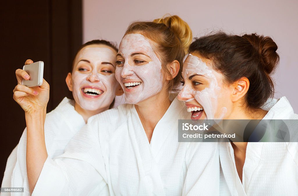 Three young happy women with face masks at spa resort. Three young happy women with face masks taking selfie at spa resort. Friendship and wellbeing concept Facial Mask - Beauty Product Stock Photo