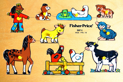 Paris, France - January 18, 2016: Horizontal composition color photography close-up of old fashioned educational game and vintage wood toy curve cut out in a wood plank, wooden flat shape sorter children's toy taken in front view full frame. There are some colored (multi colors) illustrations on this educative game with different farm animals : brown horse, chicken, duck, white and black cow, pink pig, dog, a sheep, a goat, one frog on water and a red scarecrow. It's an old Fisher Price brand toy of the 1990s for child aged one and a half to four years old. Fisher-Price is an American company that produces toys for children, headquartered in East Aurora, New York. Fisher-Price has been a wholly owned subsidiary of Mattel since 1993.