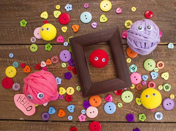 Balls of yarn with eyes and colored buttons. On wooden background.