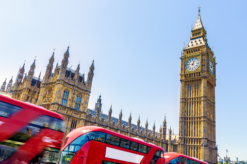 Big Ben and House of Parliament in London with red buses passing by in motion on a cloudless day