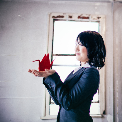 Holding it in her hands, a young Japanese woman is proudly showing the Origami swan she just made.